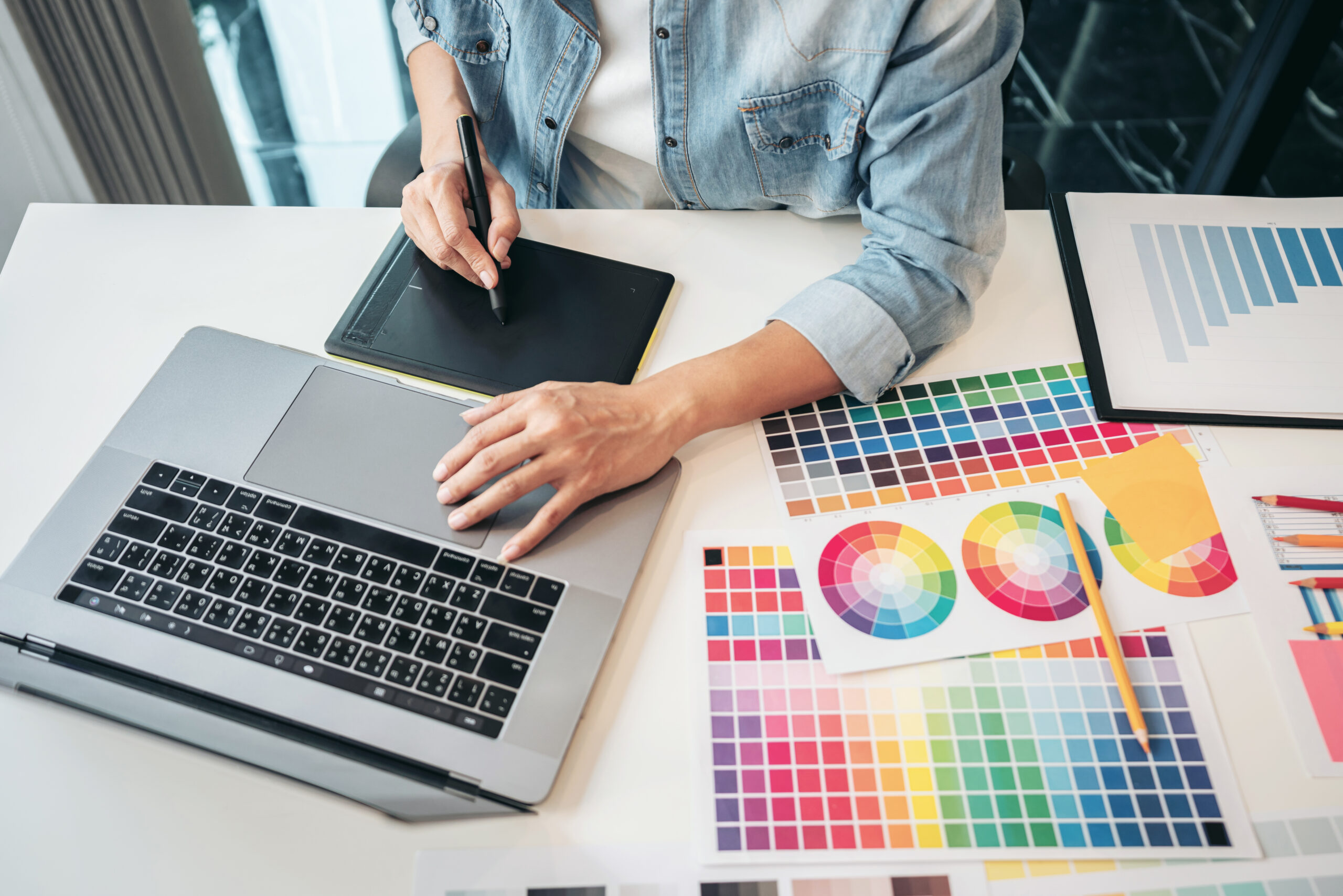 Young creative graphic designer working on color selection and drawing on graphics tablet at workplace, Color swatch samples chart for selection coloring in inspiration to create new collection.